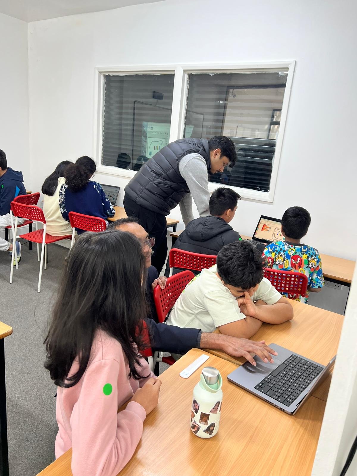 Tutor supporting children with coding activities on laptops